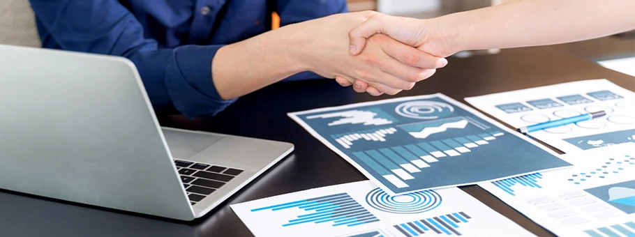 Business people shaking hands over a laptop and charts